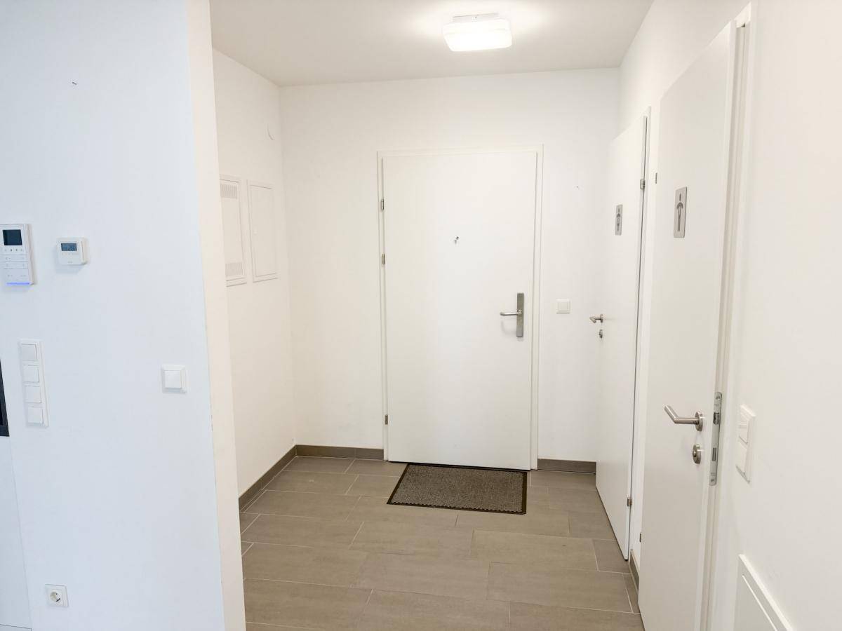 Heller Eingangsbereich mit Fliesenboden und weißen Türen, der zu den Wohnräumen führt.