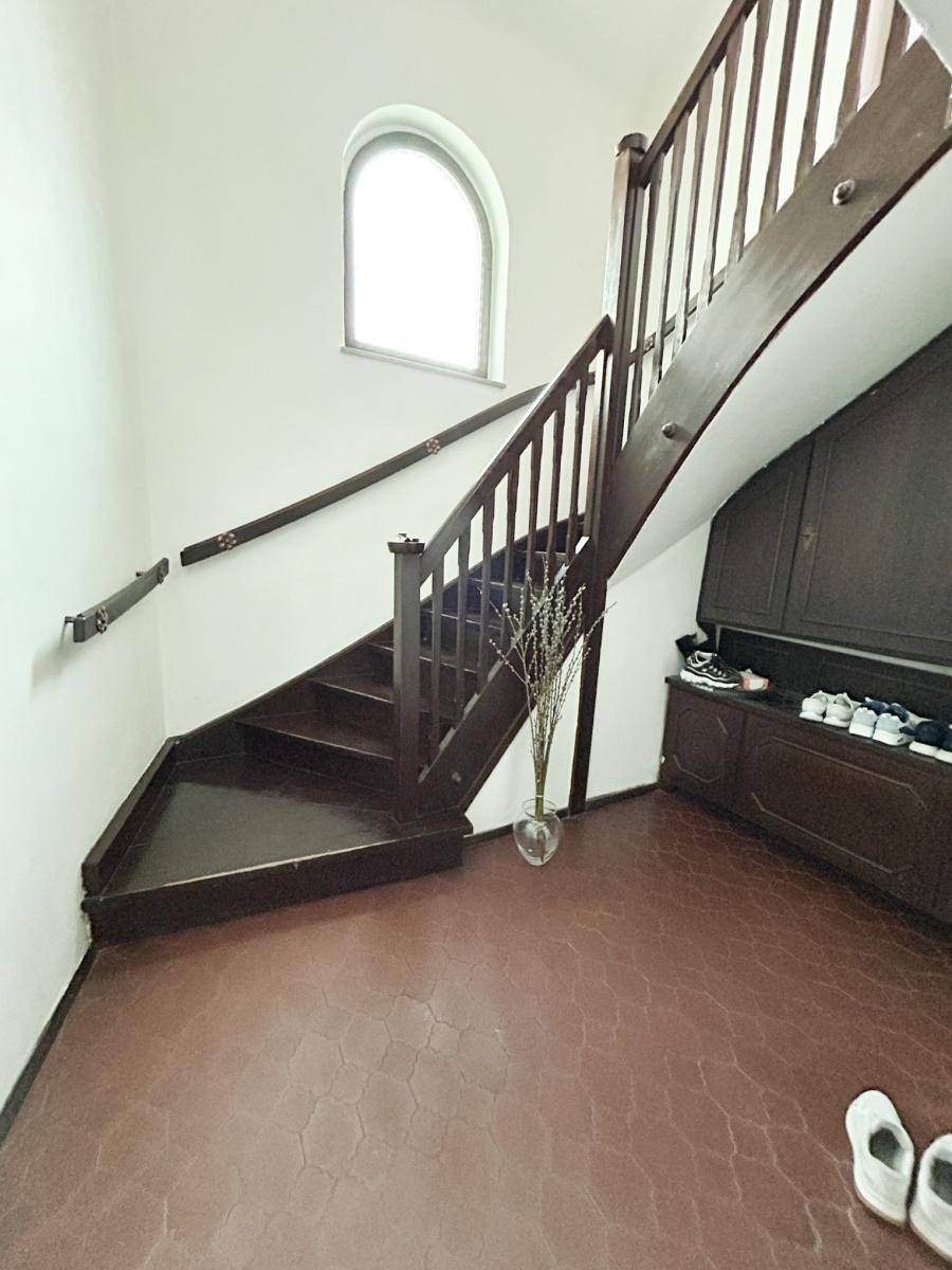 Dunkle Holztreppe in einem Flur mit gewölbtem Fenster und Ablage für Schuhe.