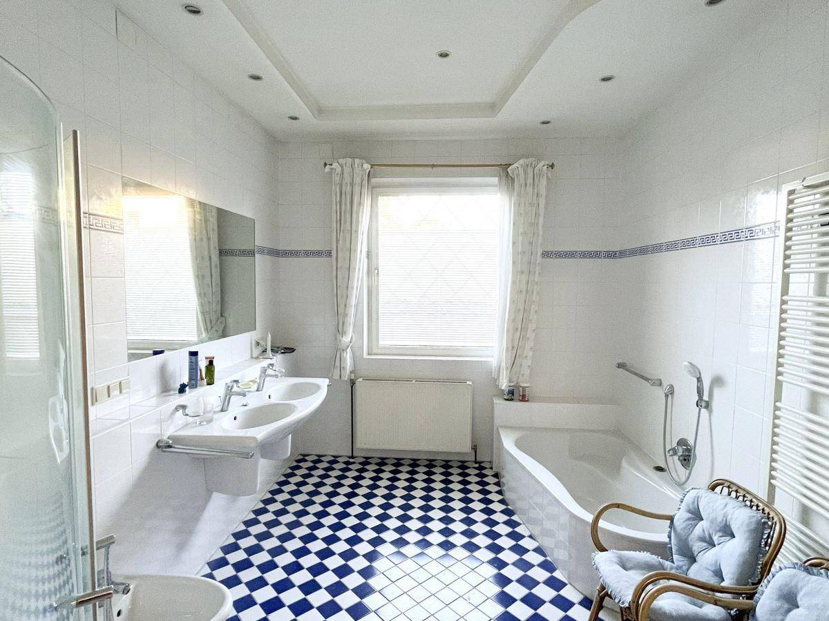 Geräumiges Badezimmer mit blau-weiß karierten Fliesen, Badewanne, Dusche und Doppelwaschbecken.