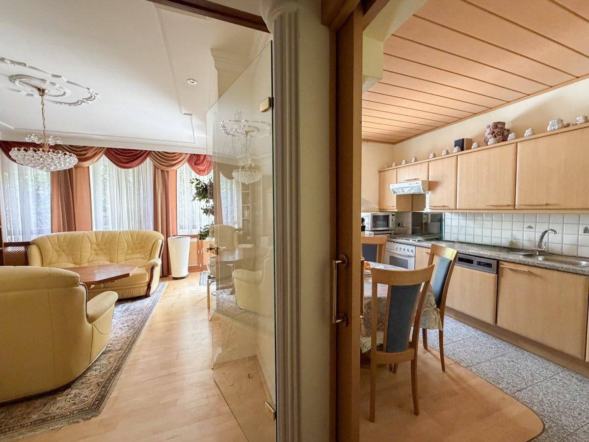 Blick vom Wohnzimmer in die angrenzende Küche, beide Räume mit traditioneller Einrichtung und Holzelementen.