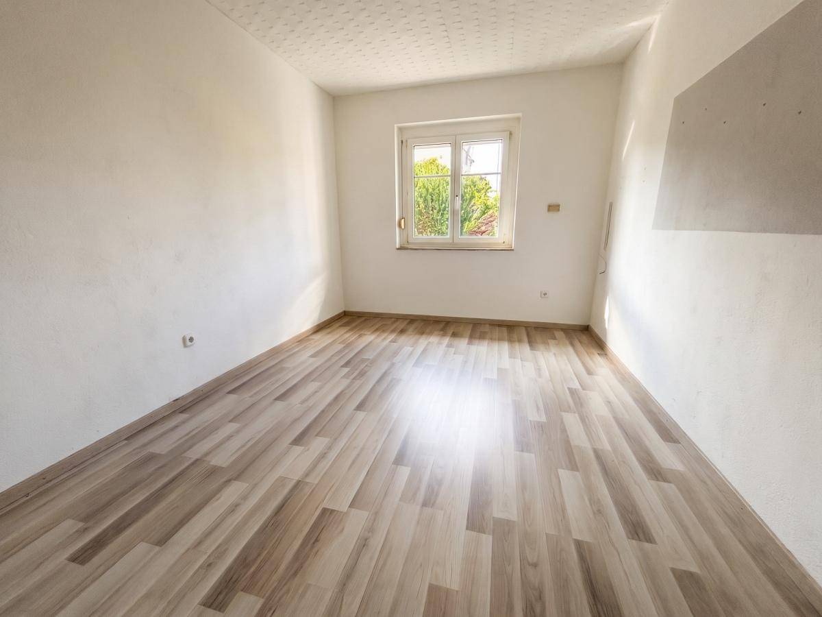 Helles Schlafzimmer mit Laminatboden und Fenster, das viel Tageslicht hereinlässt.