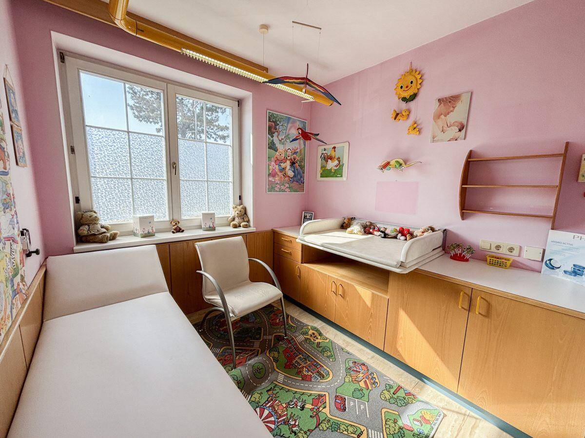 Kinderfreundlicher Raum mit Wickeltisch, Bett und Spielteppich, hell und farbenfroh gestaltet.