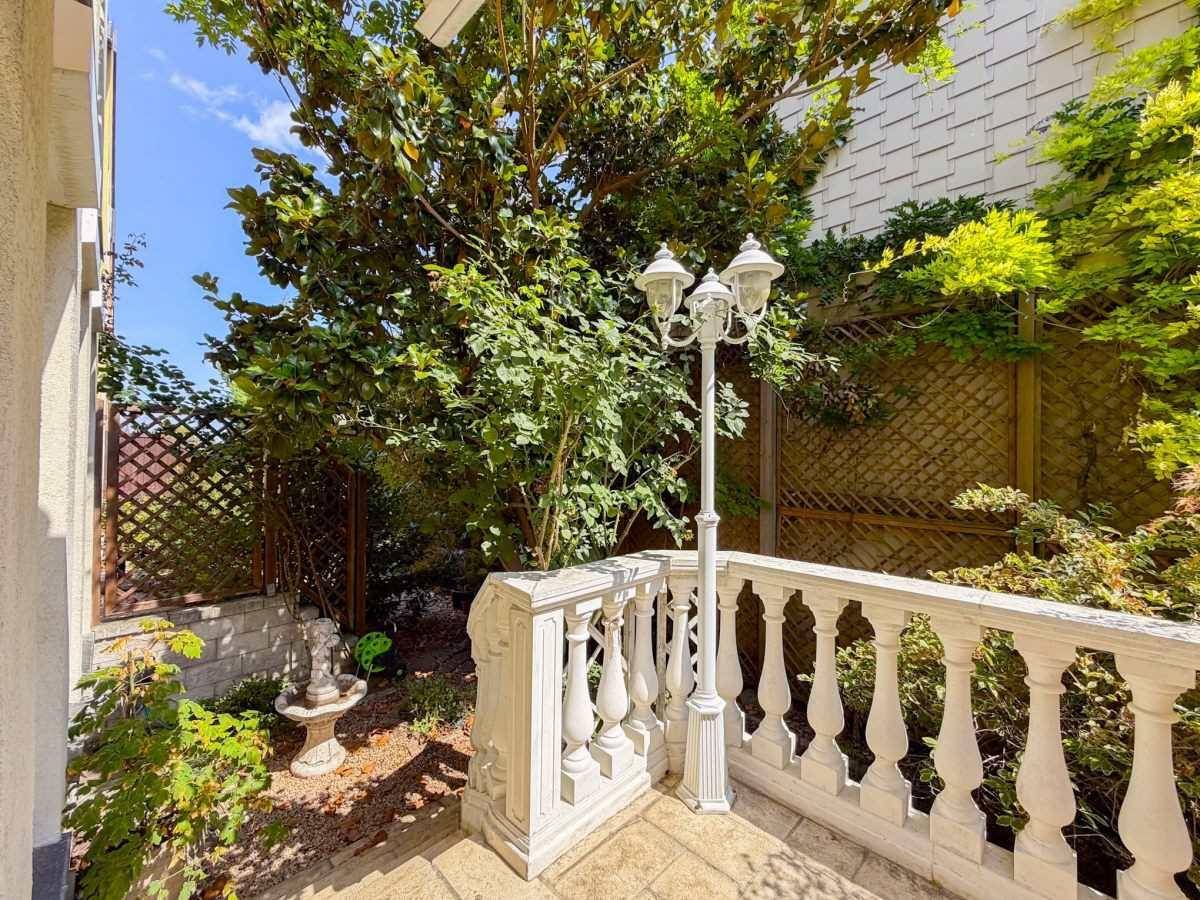 Sonniger Terrassenbereich mit klassischer Balustrade, umgeben von üppigem Grün und einem kleinen Brunnen.