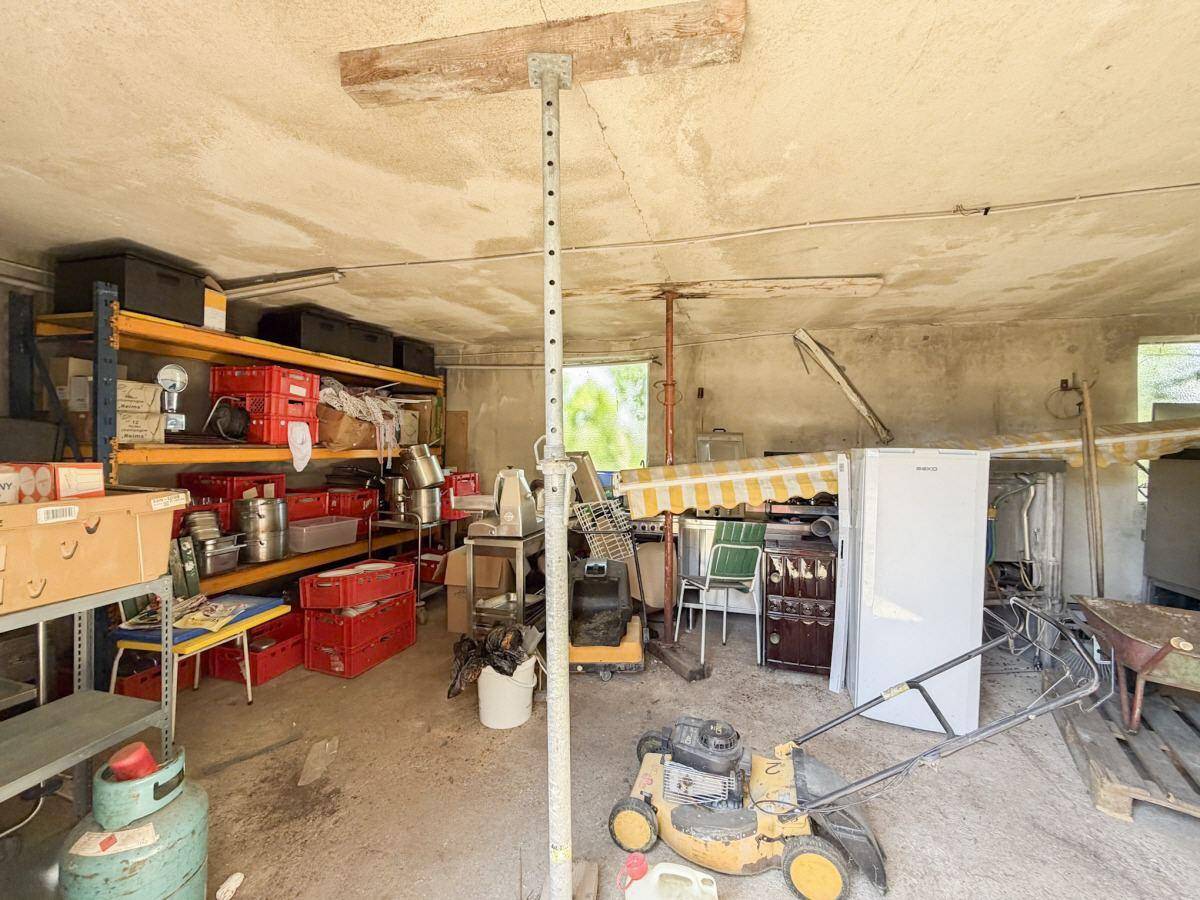 Chaotischer Lagerraum mit Regalen, Kisten, einem Rasenmäher und einem Kühlschrank.