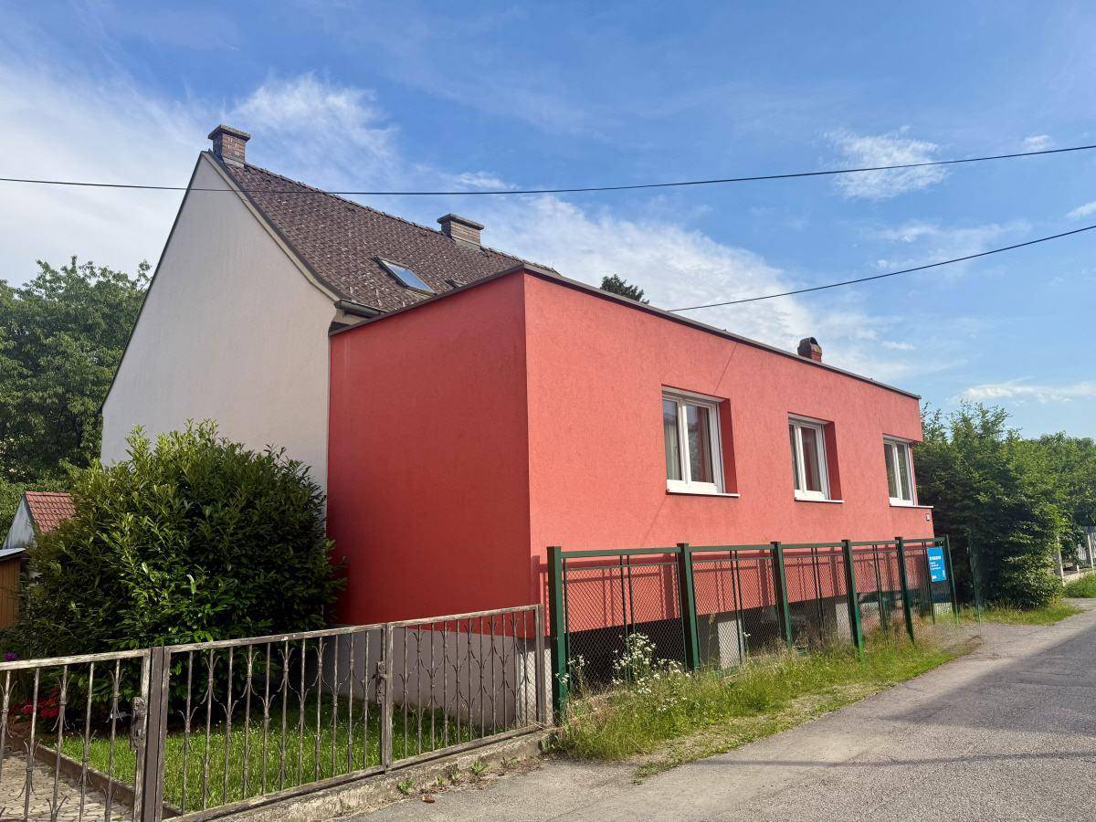 Seitenansicht des Hauses mit roter Fassade und Zaun entlang der Straße.