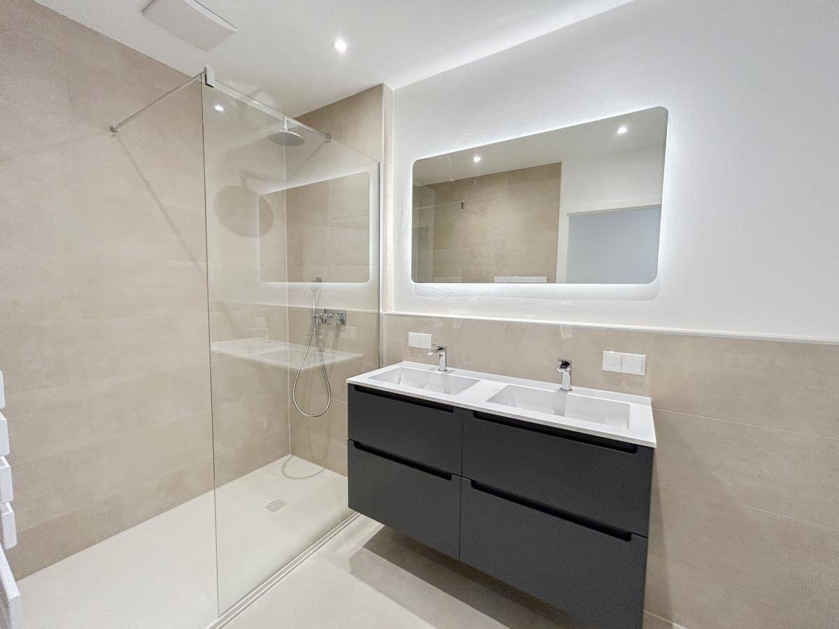Modernes Badezimmer mit Doppelwaschbecken, großer begehbarer Dusche und beleuchtetem Spiegel.