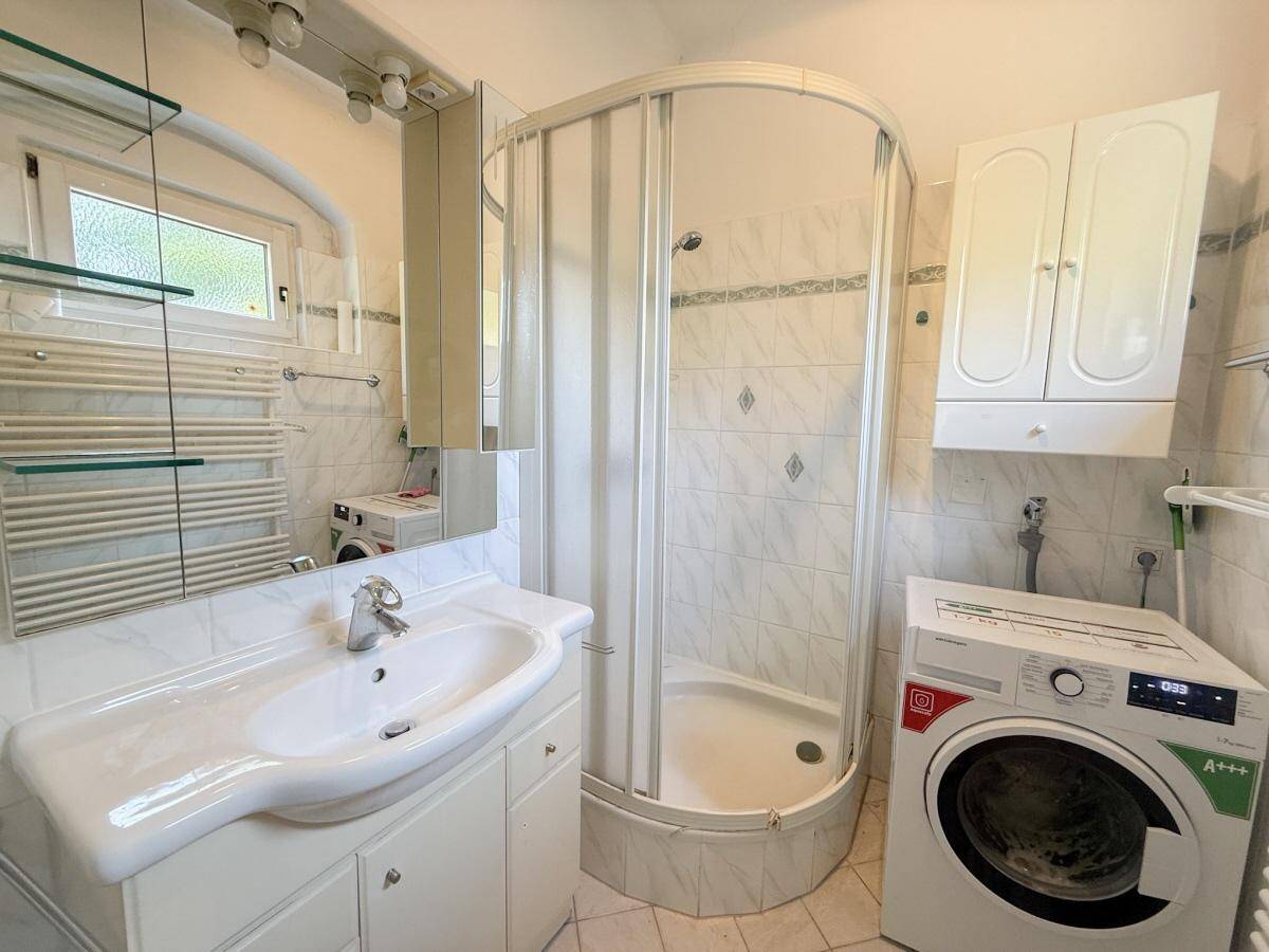 Helles Badezimmer mit Duschkabine, Waschbecken und integrierter Waschmaschine.