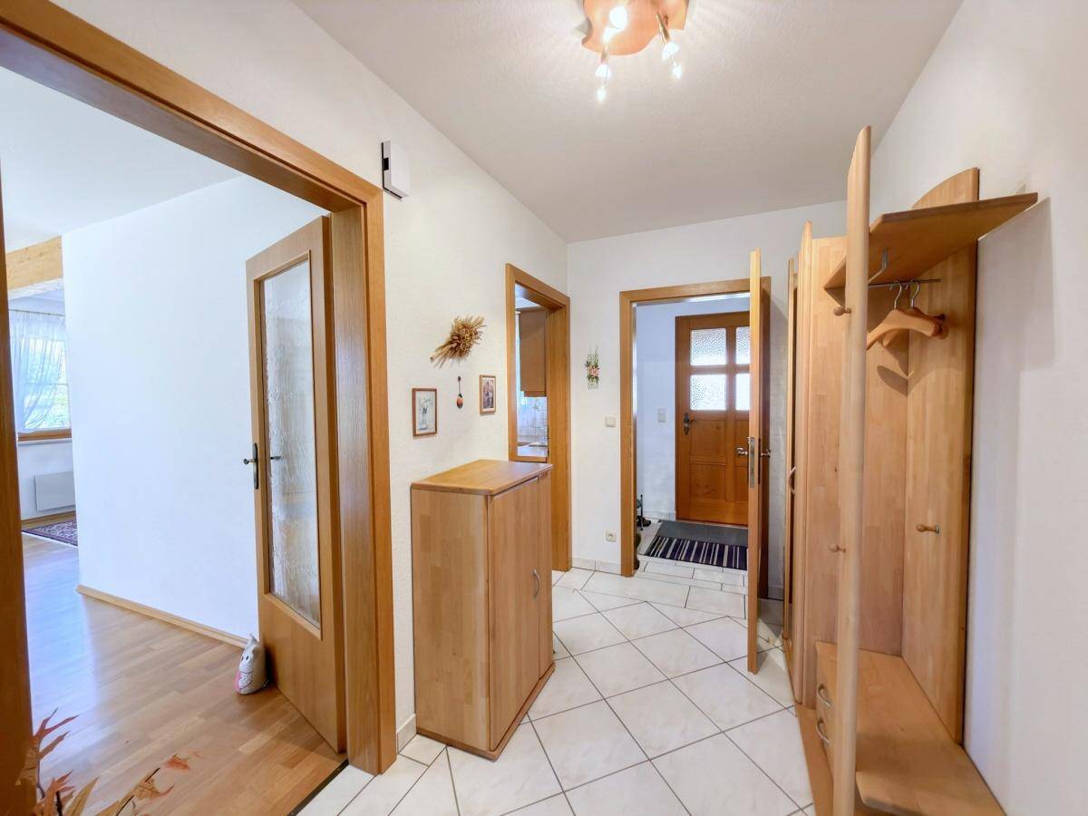 Heller Eingangsbereich mit Fliesenboden, Holzmöbeln und mehreren Türen.