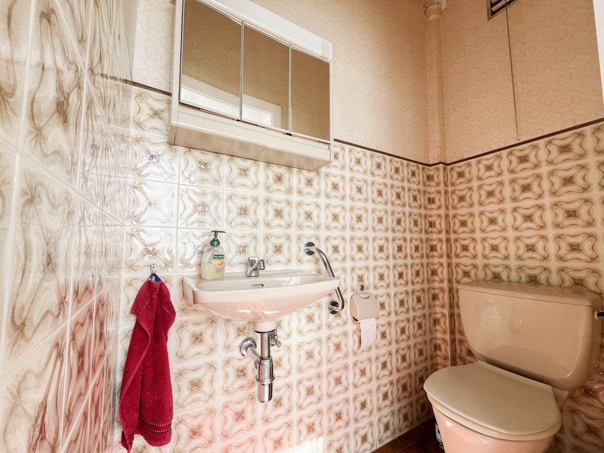 Kleines Gäste-WC mit gemusterten Fliesen, Waschbecken und Toilette in Pastellfarben.