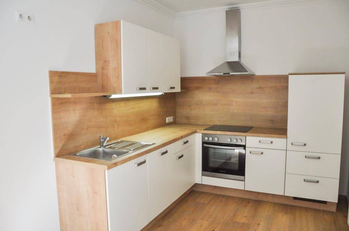 Eine moderne Einbauküche mit weißen Schränken, Holzoptik-Arbeitsplatten und integrierten Geräten.