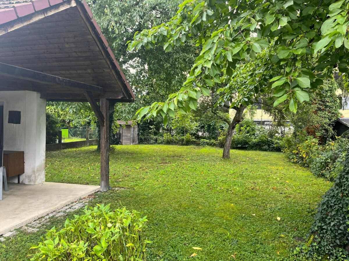 Großer, gepflegter Garten mit Rasenfläche, alten Bäumen und einem kleinen Schuppen im Hintergrund.