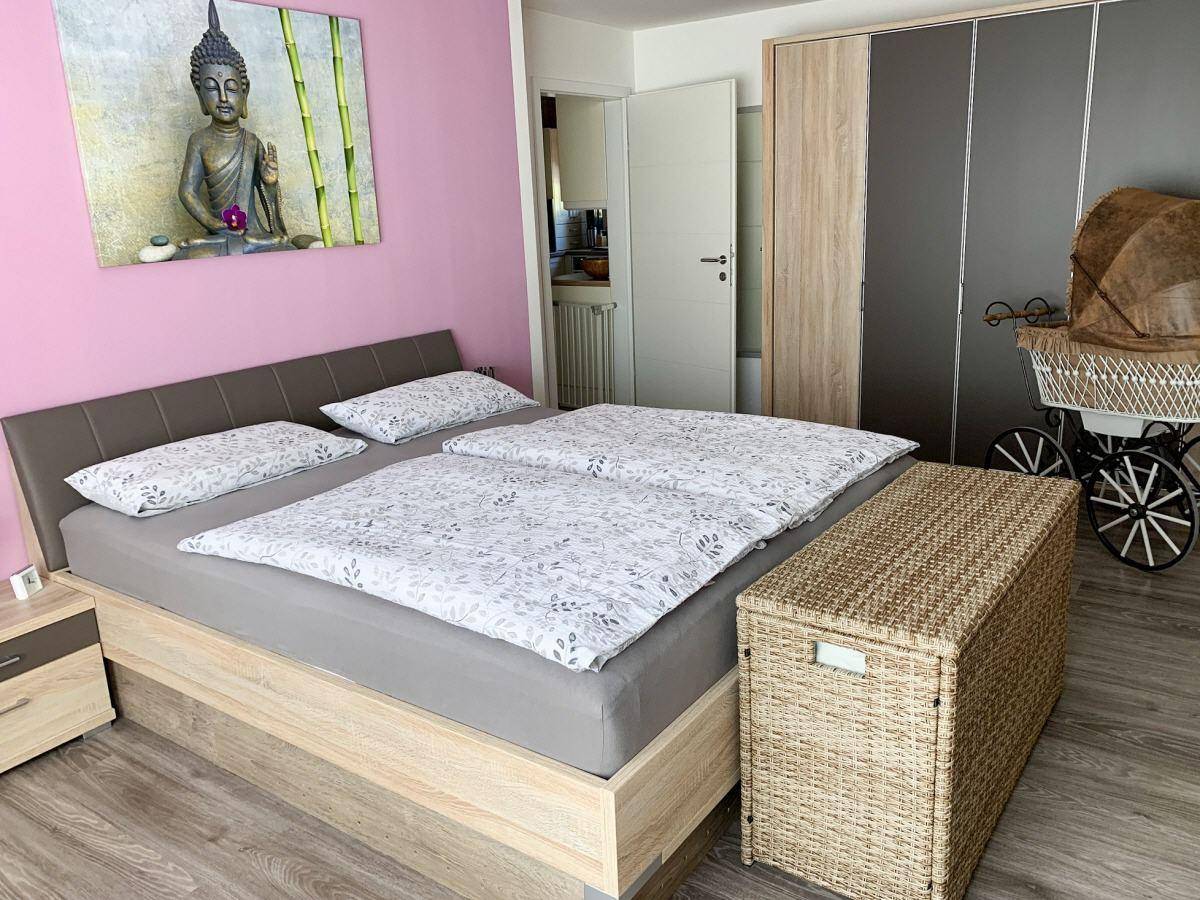 Schlafzimmer mit Doppelbett, modernem Kleiderschrank und farbiger Akzentwand in Rosa.