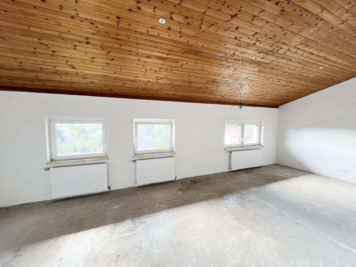 Unfertiger Raum mit Holzbalkendecke und Betonboden, bereit für den Ausbau.