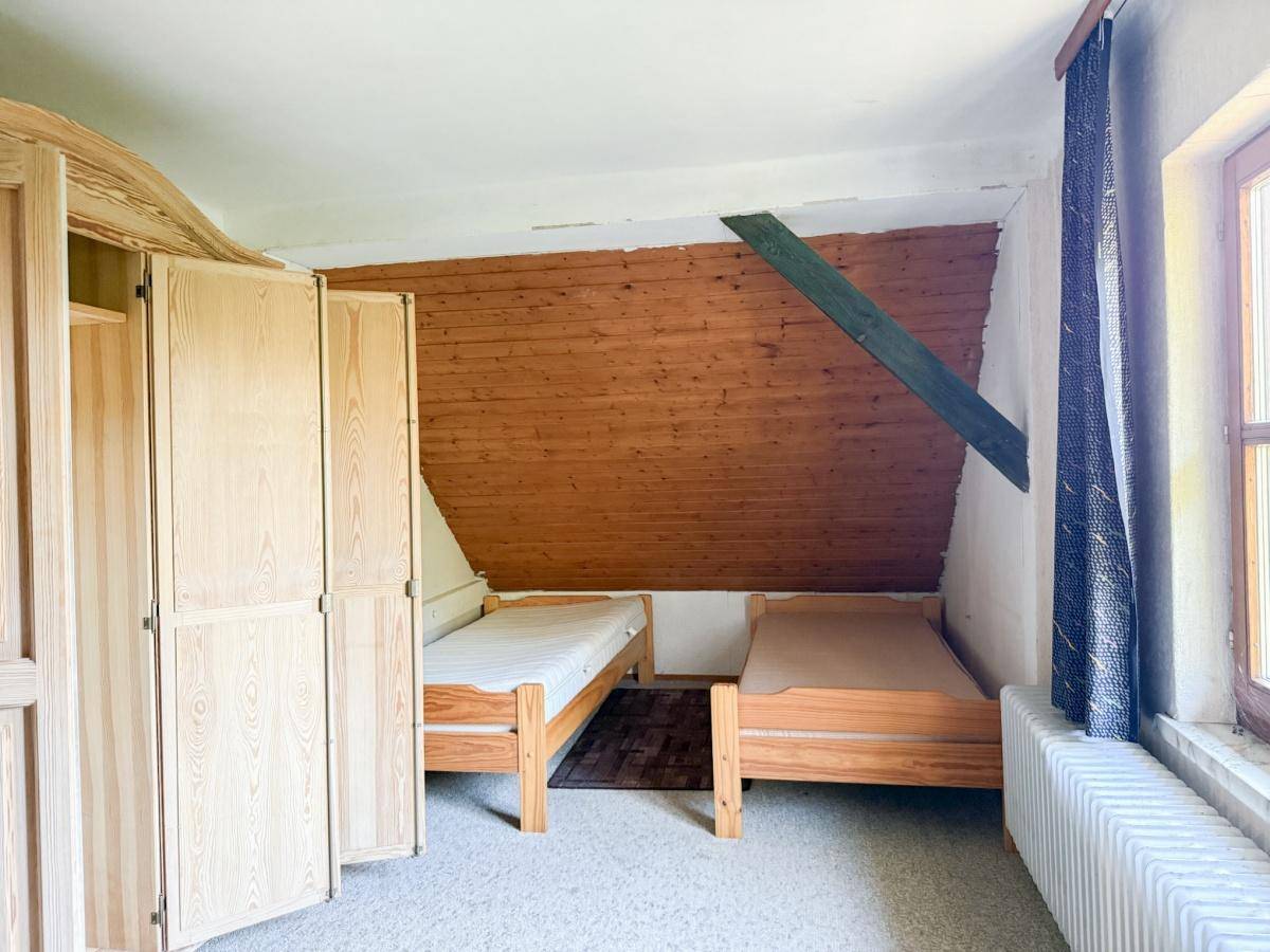 Schlafzimmer im Dachgeschoss mit zwei Einzelbetten und rustikaler Holzverkleidung an der Wand.