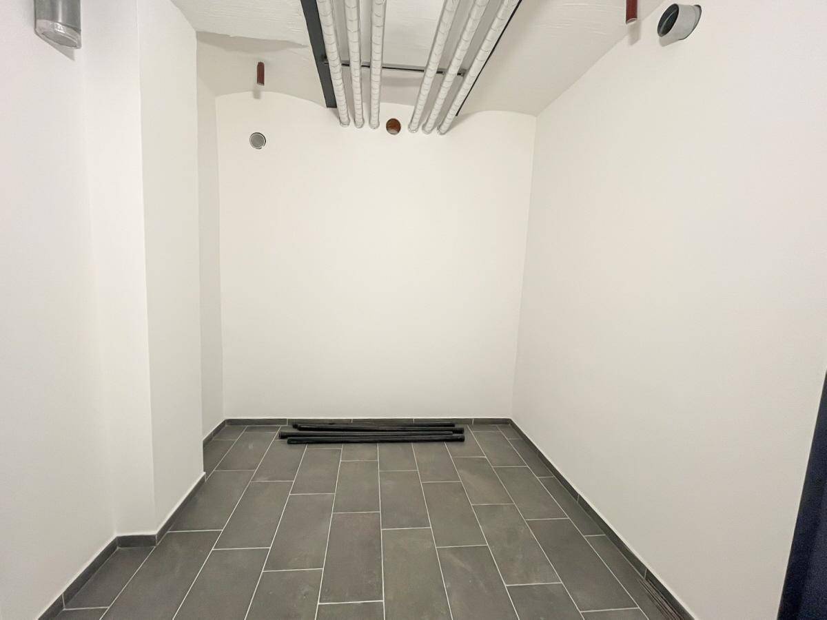 Leerer Raum mit Fliesenboden und sichtbaren Leitungen an der Decke, ideal als Abstellraum.
