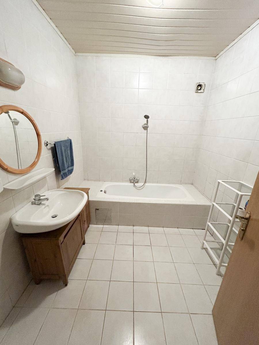 Helles Badezimmer mit Badewanne, Holzwaschtisch und weißen Wandfliesen.