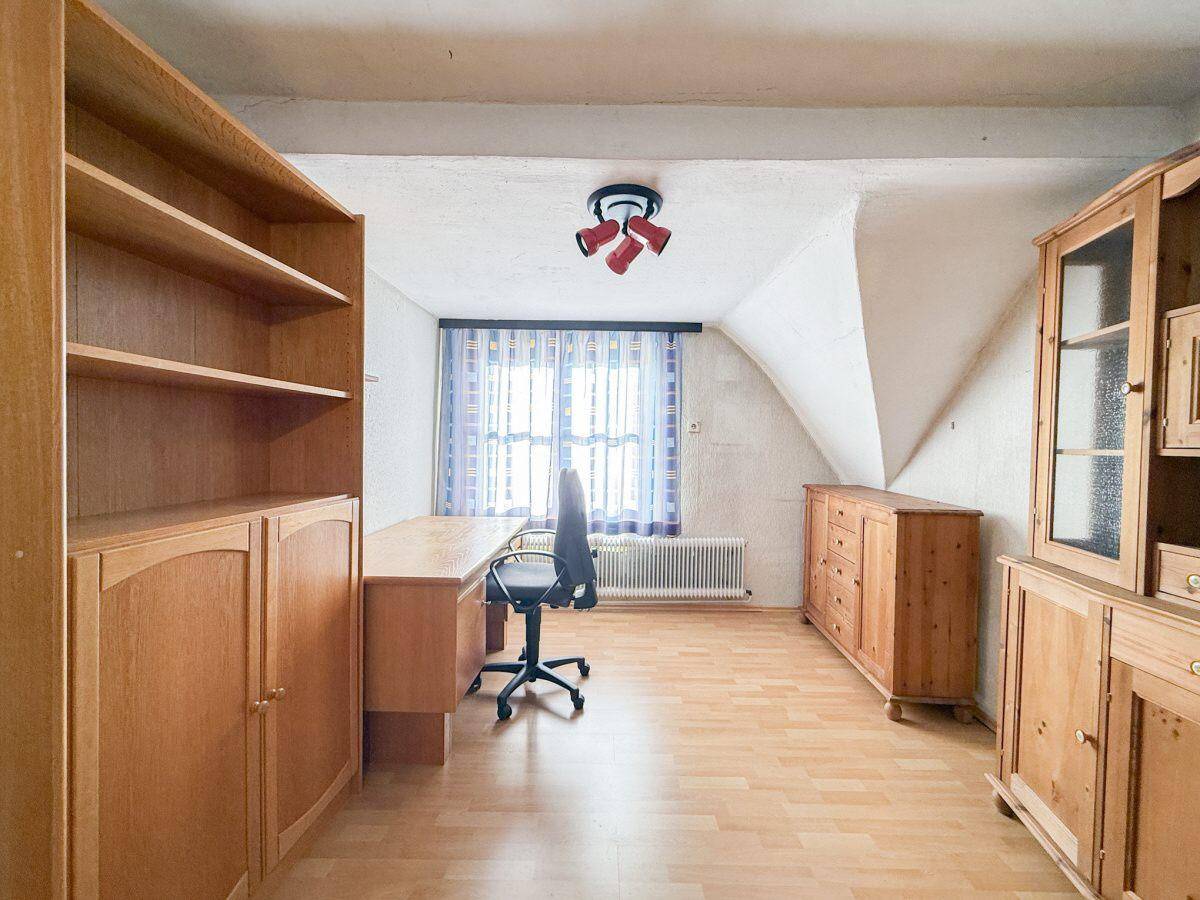 Helles Arbeitszimmer im Dachgeschoss mit Schreibtisch, Holzmöbeln und schräger Decke.