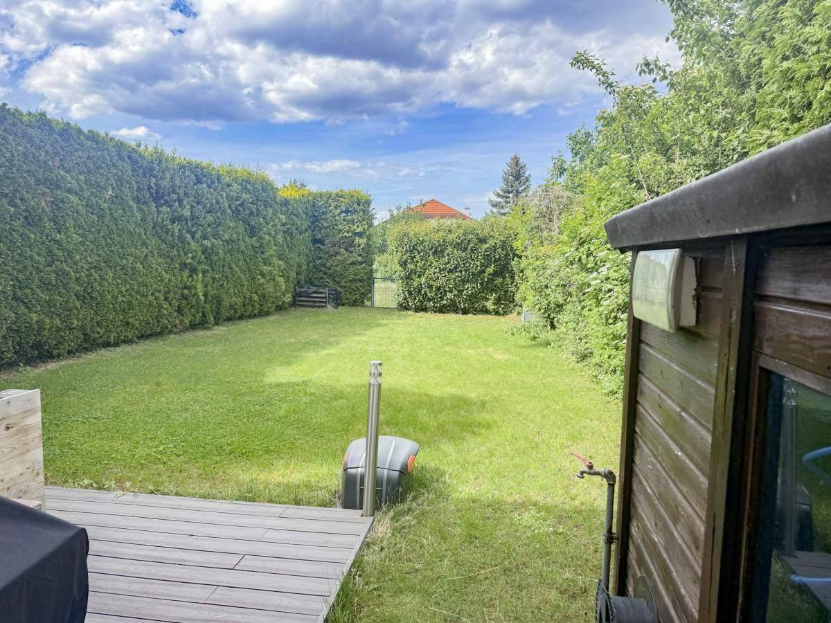 Gepflegter Garten mit Rasenfläche, Hecken und Holzterrasse, ideal zum Entspannen.