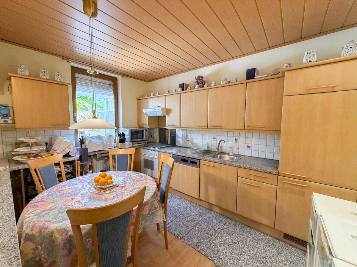 Funktionale Küche mit Holzschränken, Essbereich und gefliestem Boden unter einer Holzdecke.