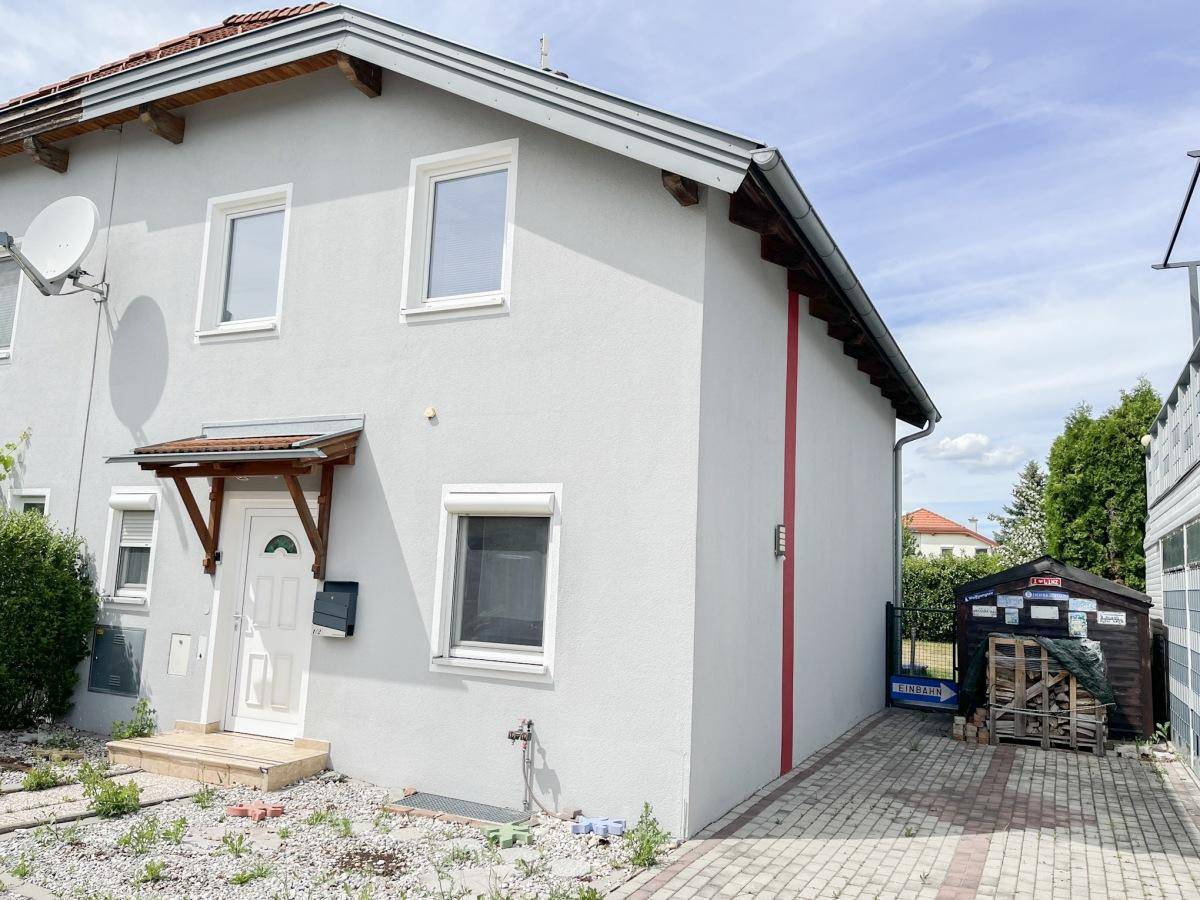 Graue Hausfassade mit Einfahrt und Gartenhaus, seitlicher Blick auf das Gebäude.