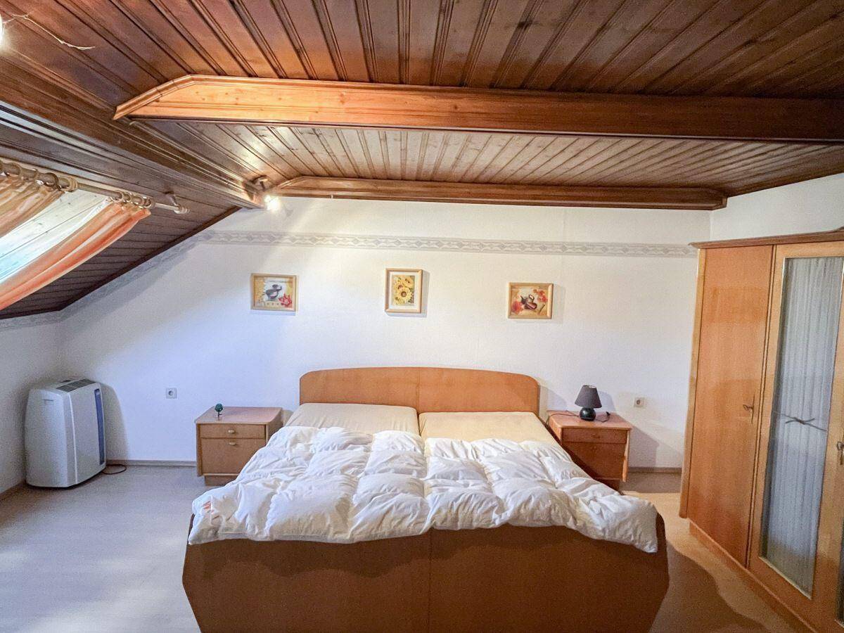 Schlafzimmer im Dachgeschoss mit Holzbalkendecke, Doppelbett und Dachschräge, hell und geräumig.