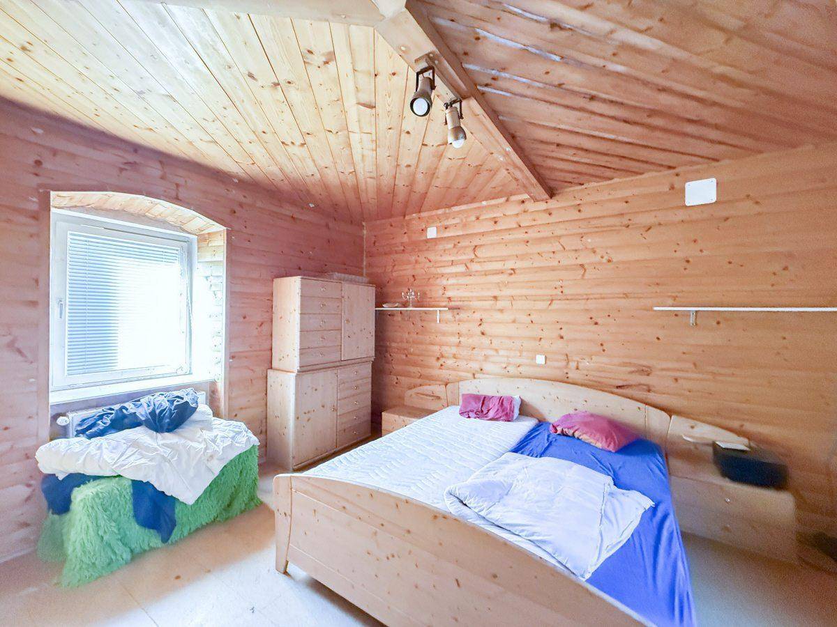 Gemütliches Schlafzimmer mit Holztäfelung an Wänden und Decke, einem Holzbett und schrägen Dachflächen.