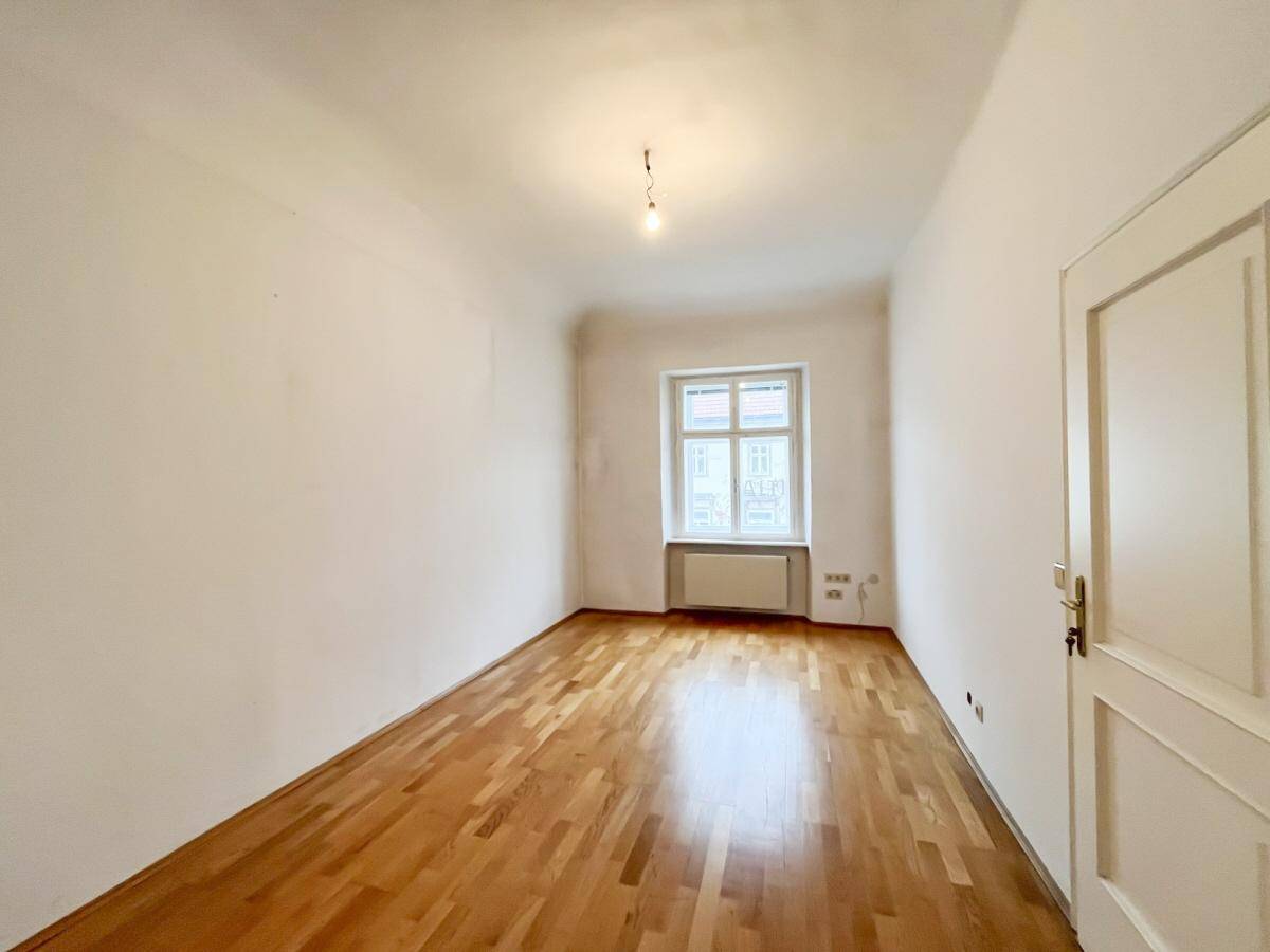 Leeres Zimmer mit weißen Wänden, Holzboden und einem Fenster, das den Raum hell und einladend macht.