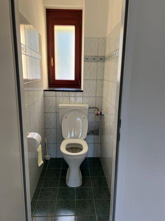 Separate Toilette mit Fenster, gefliesten Wänden und dunklem Fliesenboden.
