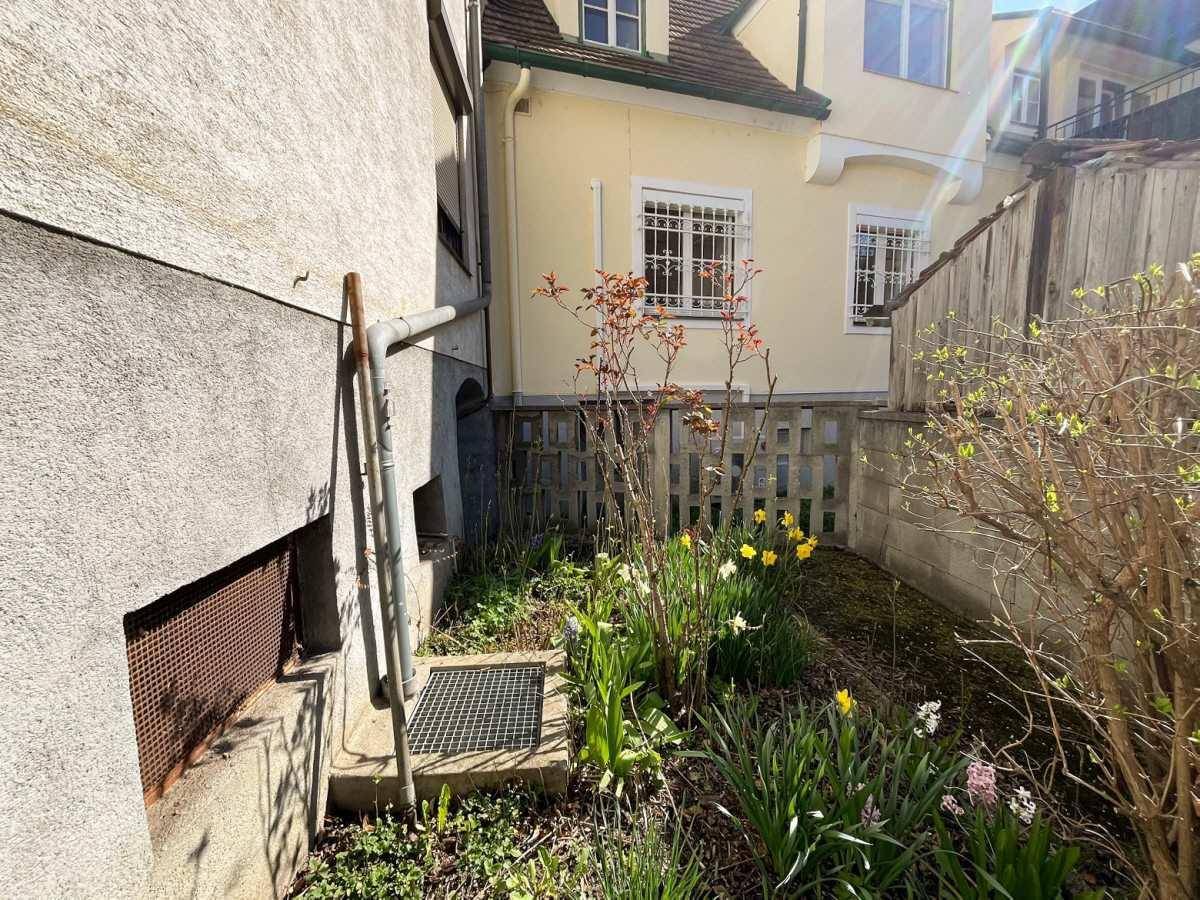 Kleiner Gartenbereich mit Frühlingsblumen und einem Gitterzaun neben dem Haus.