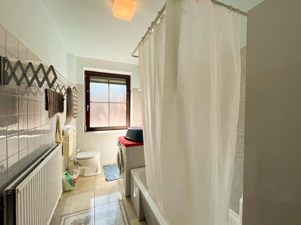 Badezimmer mit Badewanne, Fliesenboden und einem Fenster für Tageslicht.