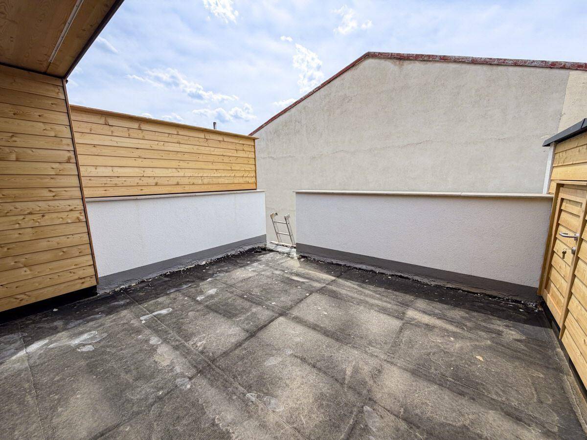 Dachterrasse im Rohzustand mit niedrigen Mauern und Blick auf die umliegenden Gebäude.