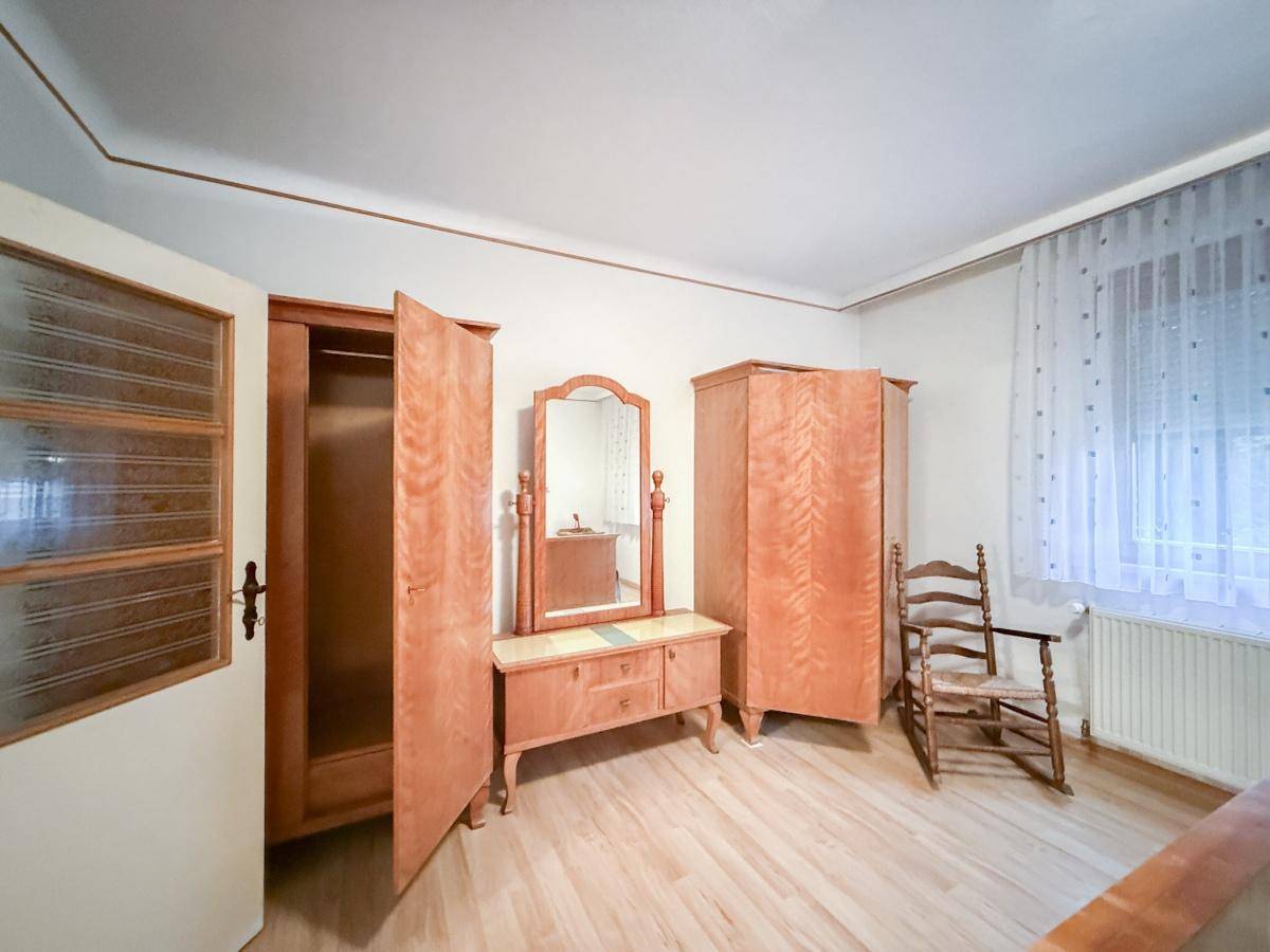 Schlafzimmer mit Holzschränken, Frisiertisch mit Spiegel und Schaukelstuhl, heller Holzfußboden.