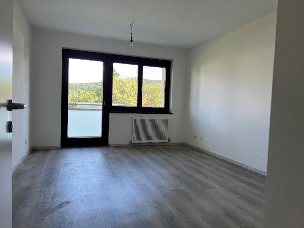 Geräumiges Wohnzimmer mit Laminatboden und großem Fenster, das Zugang zu einem Balkon bietet.