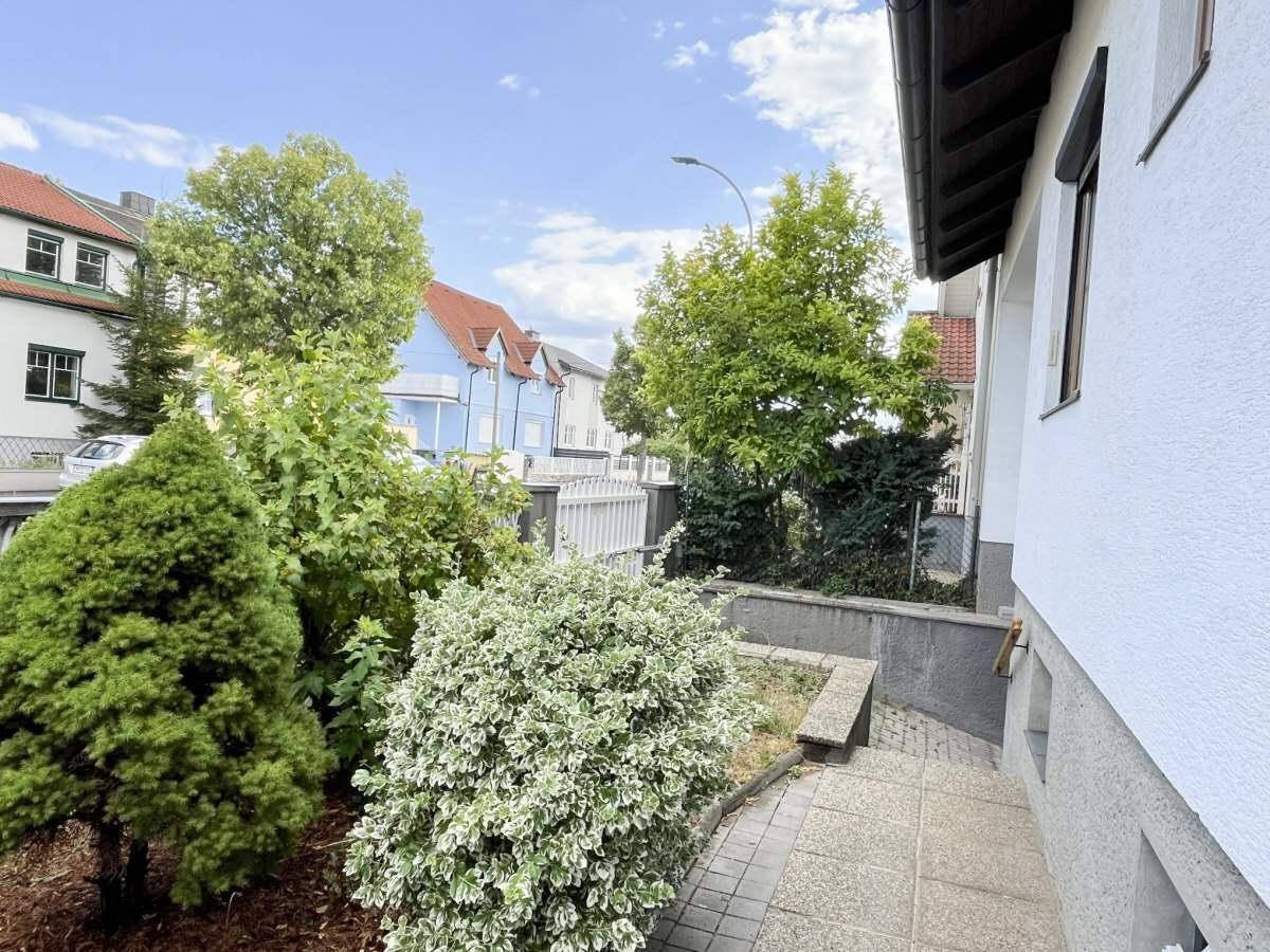 Vorgarten mit verschiedenen Sträuchern und einem gepflasterten Weg zur Haustür.