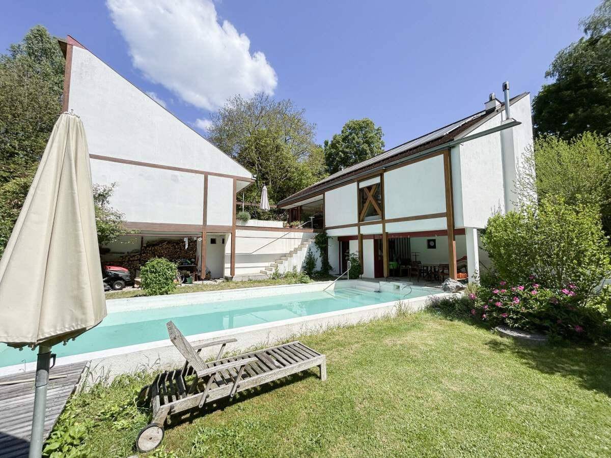 Außenansicht des Hauses mit großem Pool und weitläufigem Garten unter blauem Himmel.