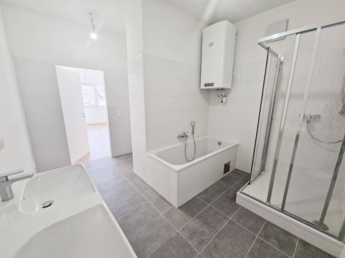 Modernes Badezimmer mit Badewanne, Dusche und Doppelwaschbecken in hellen Farben.