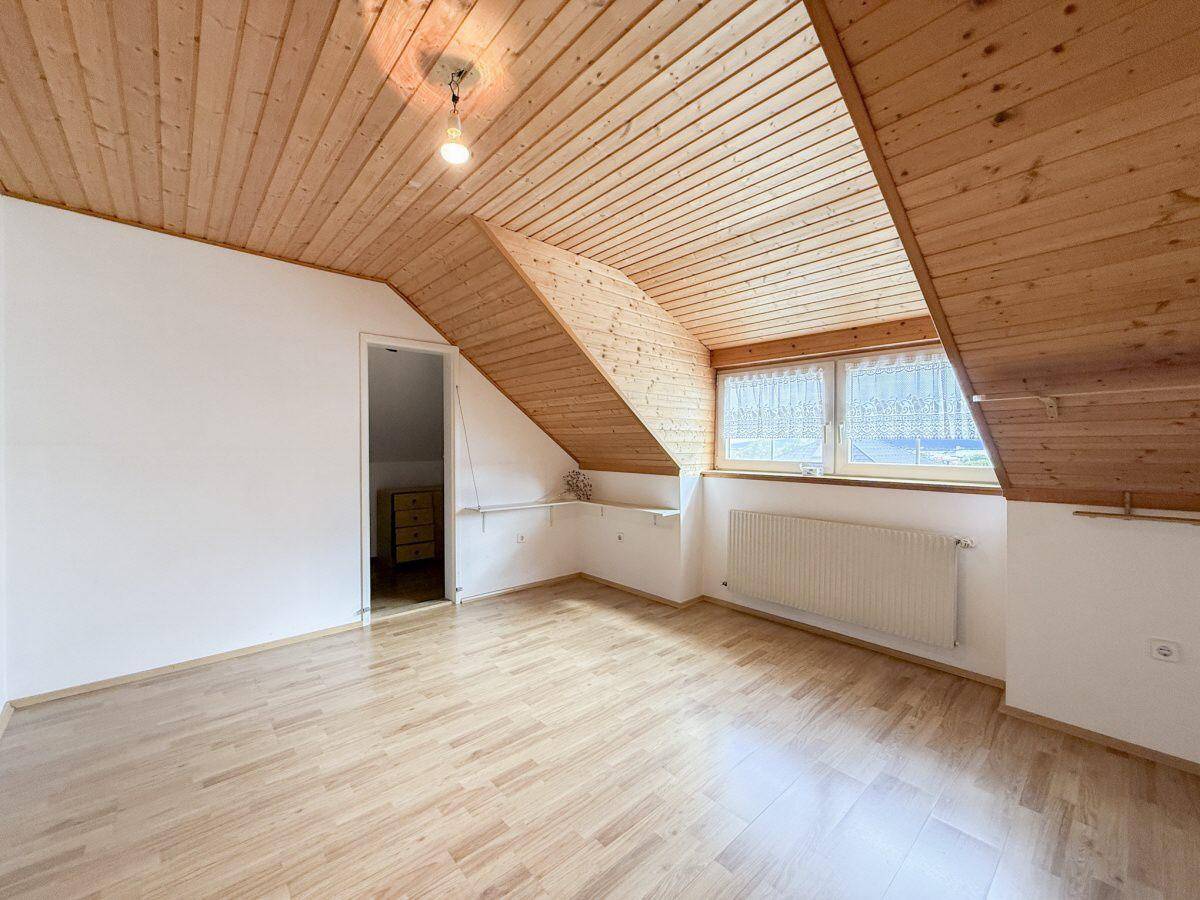 Dachzimmer mit schrägen Holzdecken, Holzboden und einem Fenster.