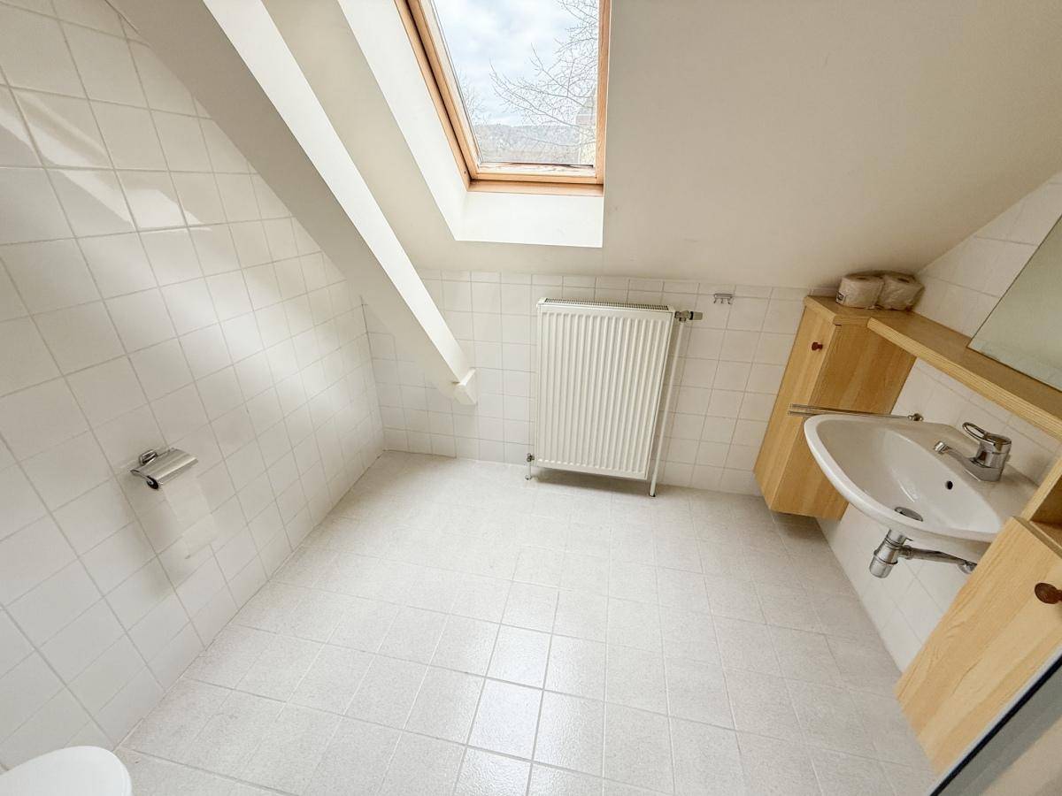 Helles Badezimmer im Dachgeschoss mit weißen Fliesen, Waschbecken und Dachfenster.