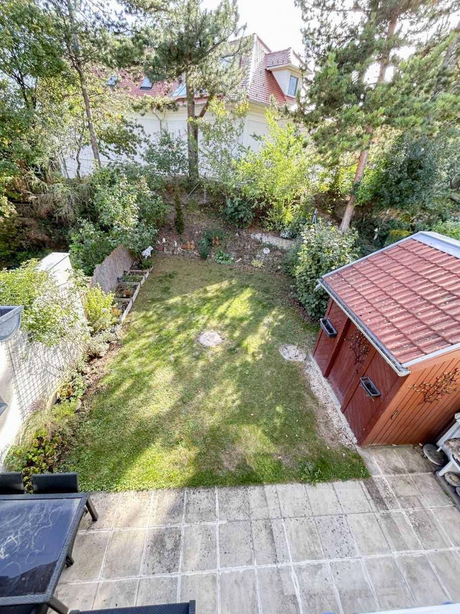 Blick von der Terrasse auf den grünen Garten mit Gartenhütte und Bäumen.