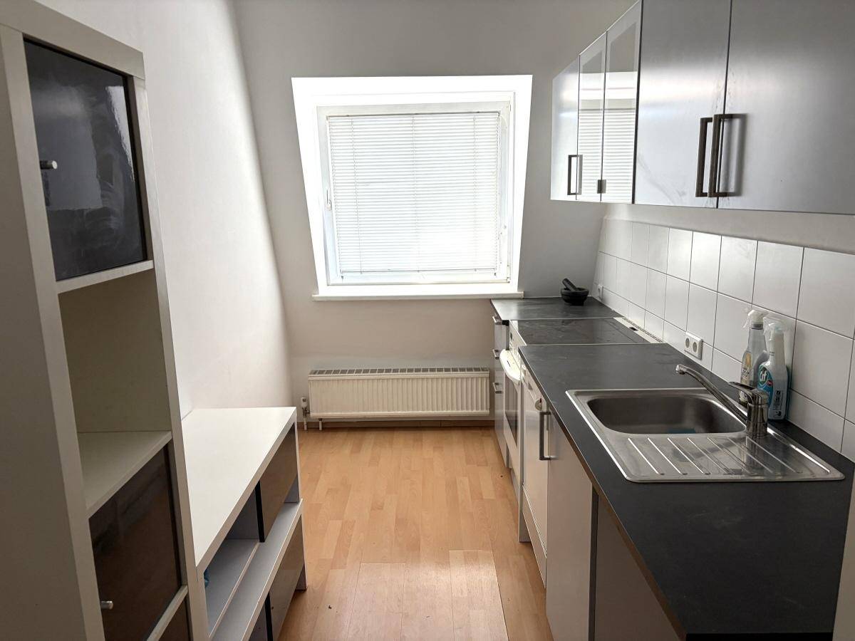 Kleine Küche mit Dachschrägen, Einbauschränken, Spüle und hellem Fenster.