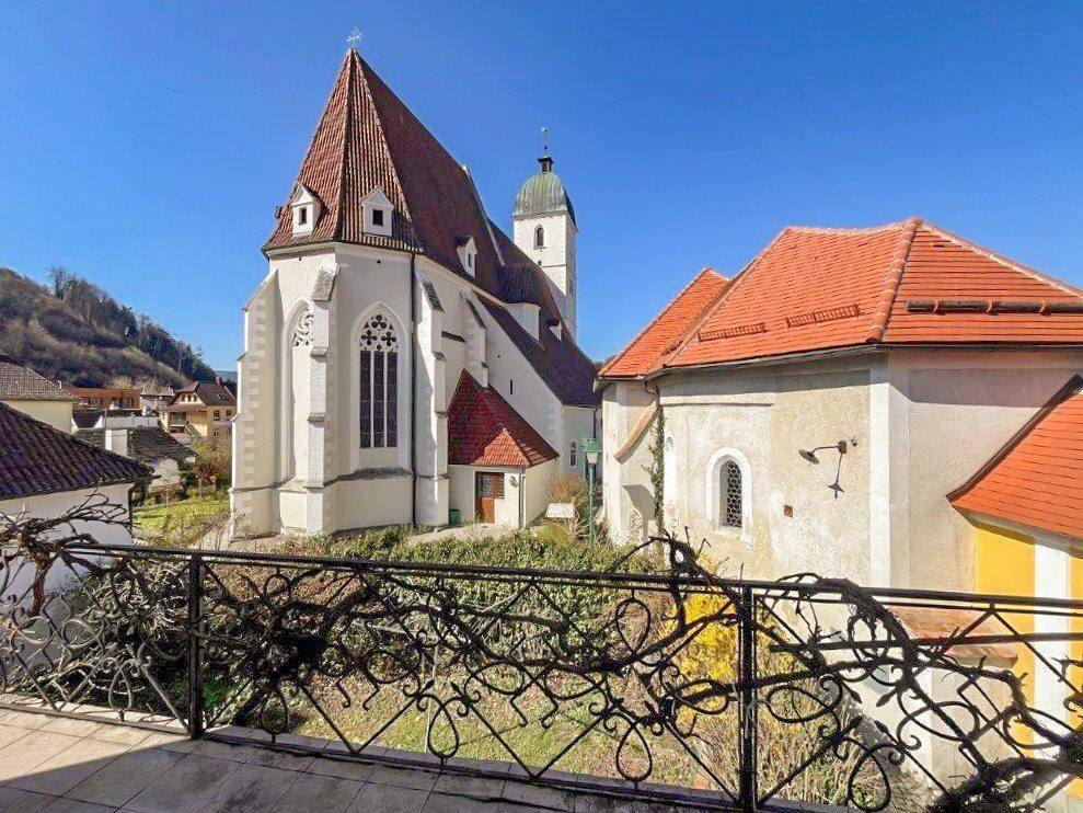 Ausblick von einem Balkon auf eine historische Kirche und die umliegende Landschaft.