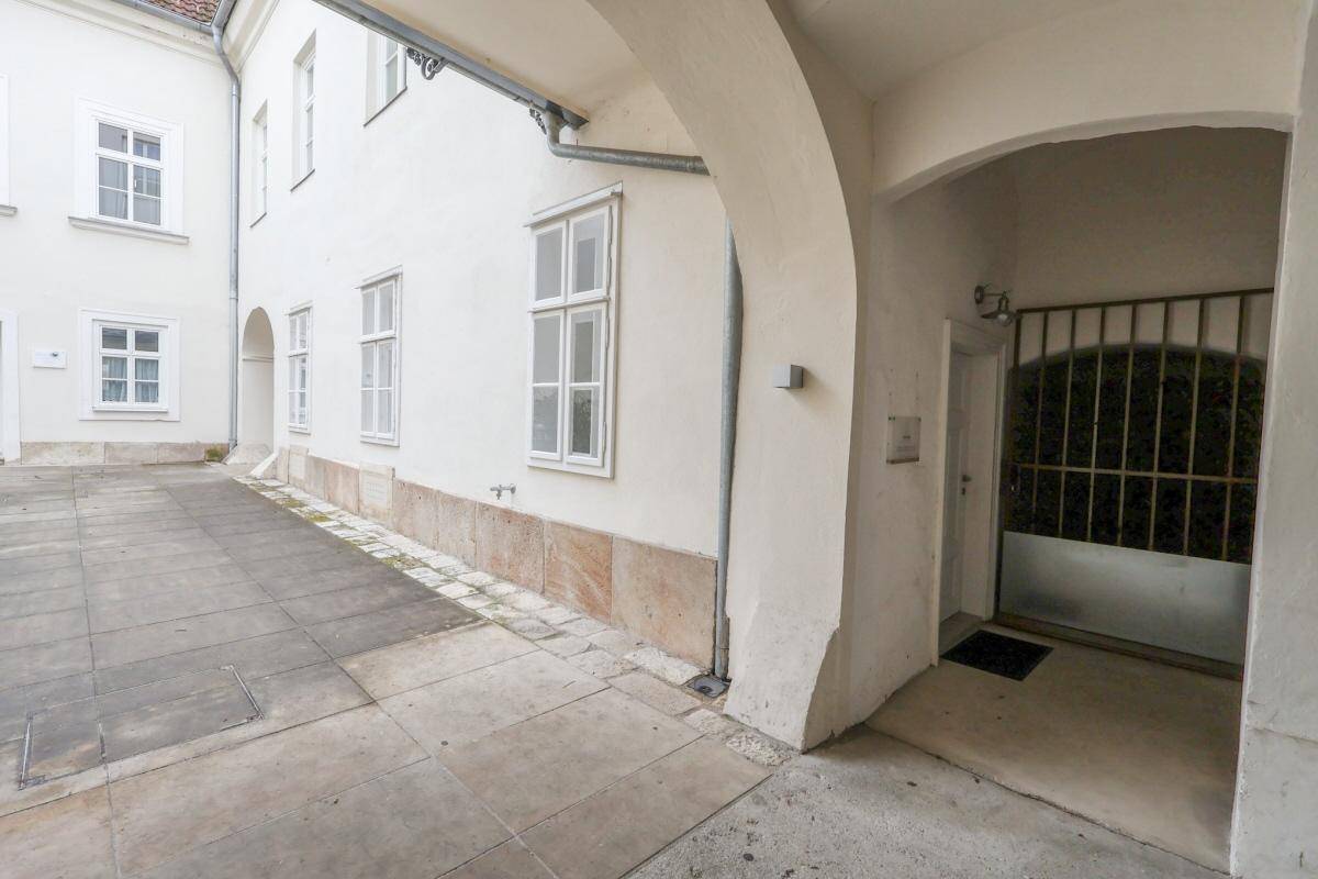 Eingangsbereich zu einem Innenhof mit gepflastertem Boden und einem Tor.