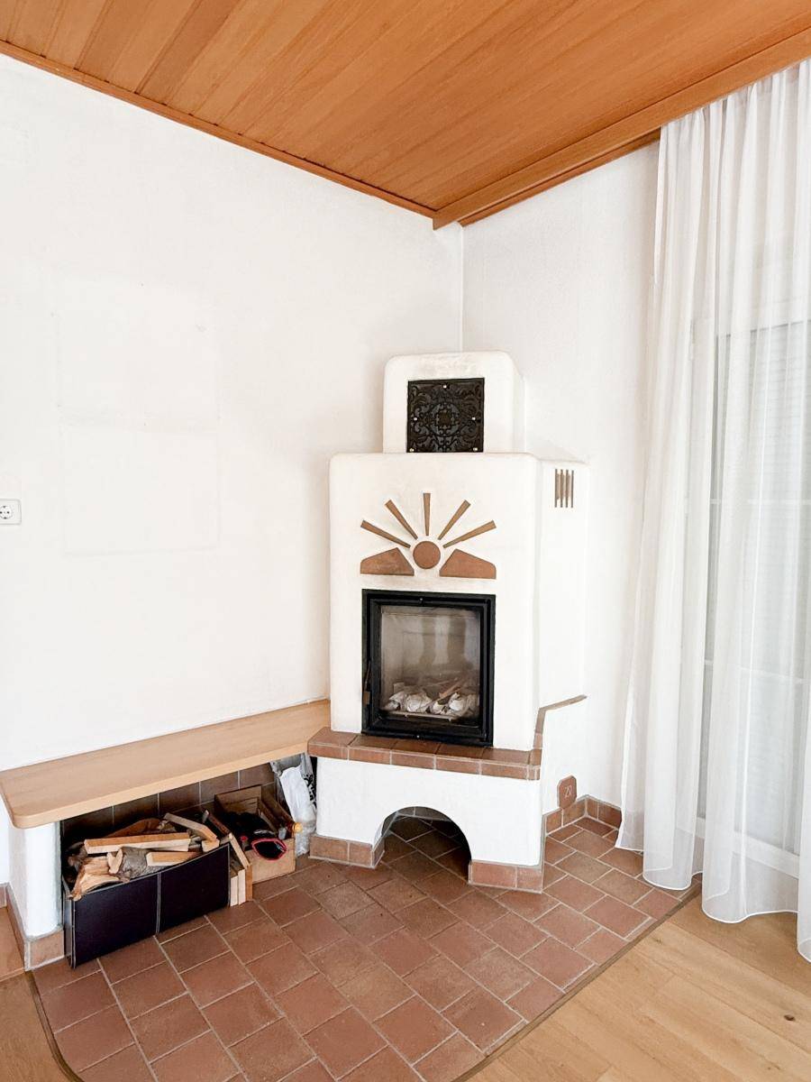 Gemütliche Ecke mit traditionellem Kachelofen, Terrakottafliesen und Holzdecke.