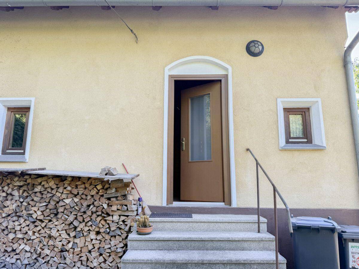 Eingangsbereich des Hauses mit Steintreppe und gestapeltem Brennholz daneben.