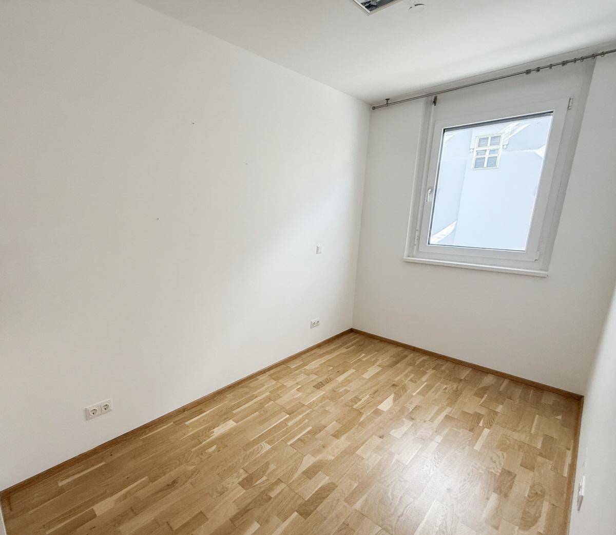 Kleiner, heller Raum mit Parkettboden und einem Fenster, ideal als Schlaf- oder Arbeitszimmer.
