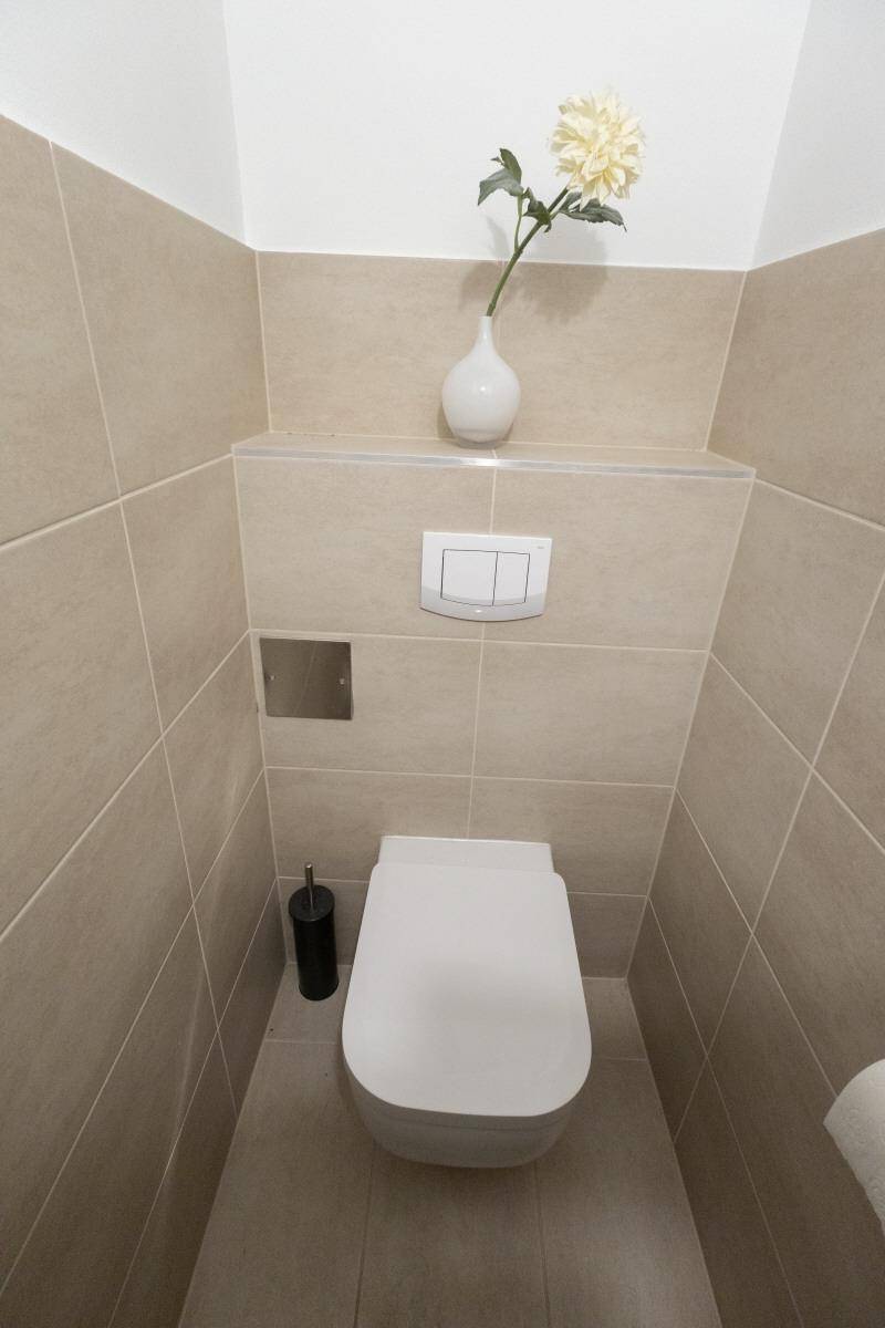 Separates WC mit wandhängender Toilette und beigefarbenen Fliesen.