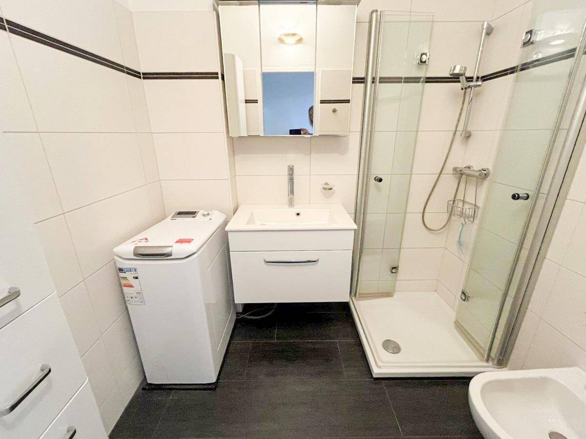 Modernes Badezimmer mit Dusche, Waschbecken und Waschmaschine, ausgestattet mit dunklen Bodenfliesen.