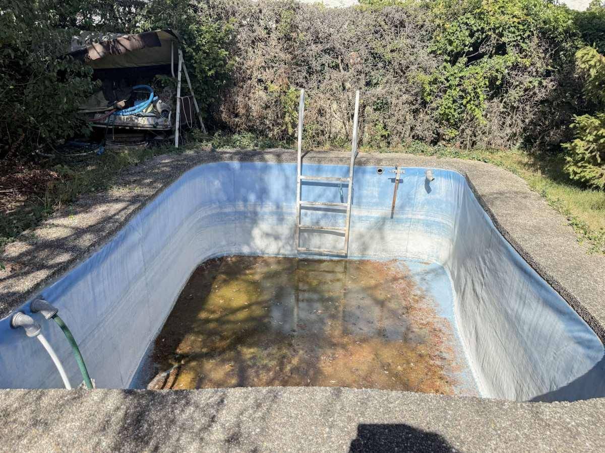 Leeres Schwimmbecken im Garten, das eine Renovierung benötigt.