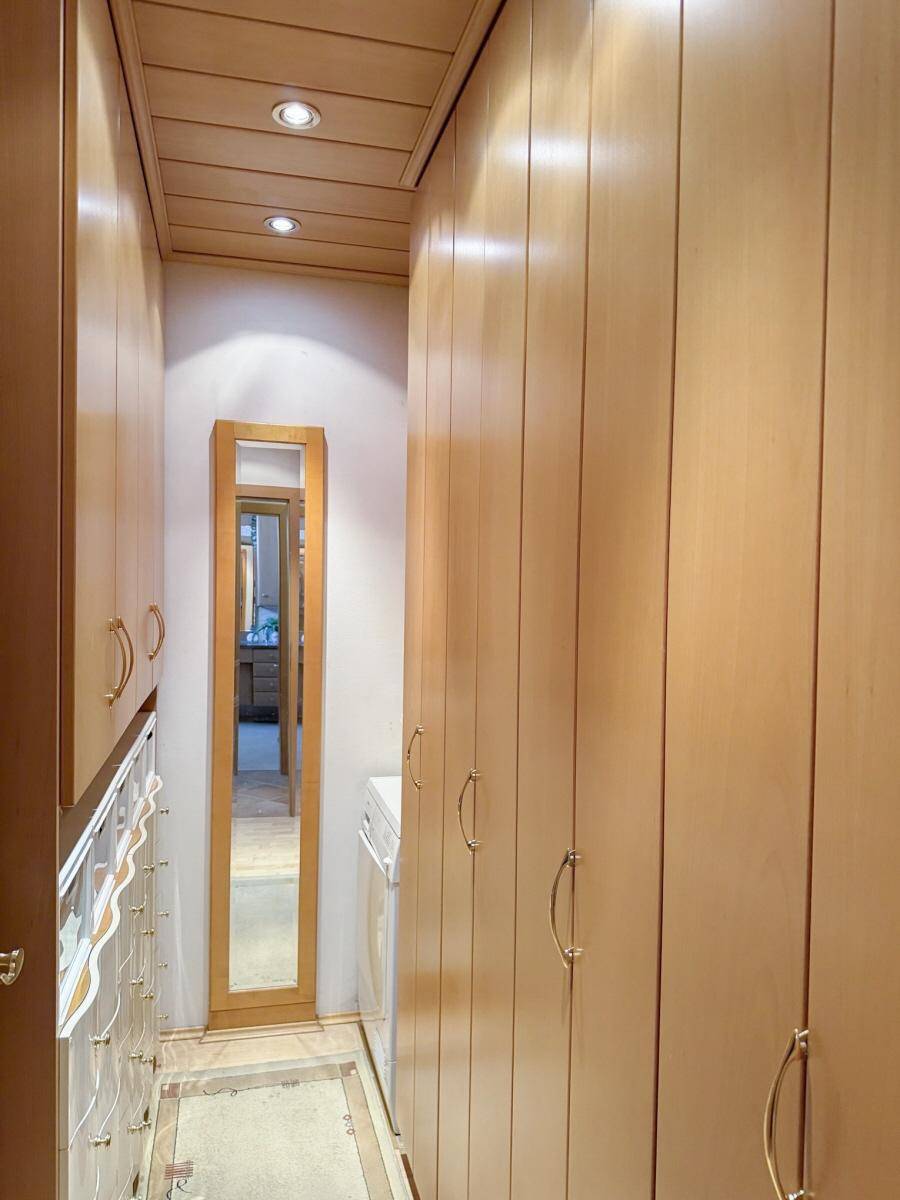 Praktischer begehbarer Kleiderschrank mit vielen Holzschränken und integrierter Beleuchtung.
