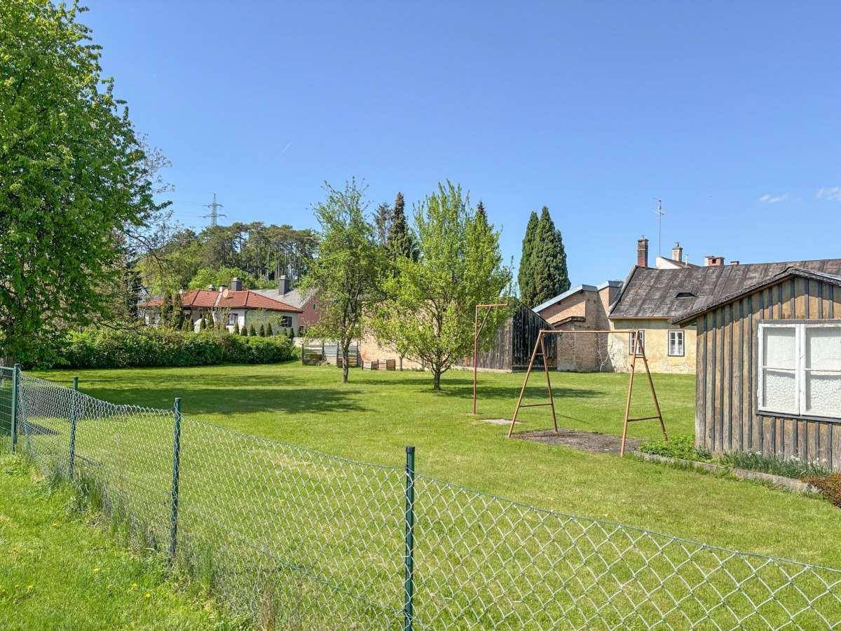 Weitläufiger Gartenbereich mit Rasenfläche, Bäumen, einem Schaukelgerüst und Blick auf die Umgebung.